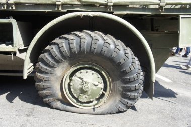A punctured and flat tire of military equipment of the armored personnel carrier. Military conflict, the shelling of the wheel. Close-up. Punctured tire of a military off-road vehicle