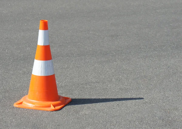 traffic cone, with white and orange stripes on gray asphalt, copy space. Bright sunny weather