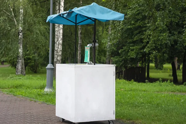Decorated lemonade stand in park. Summer refreshing natural drink. White lemonade stall with tent and cranes. White street stall on wheels lemonade taps. A barrel of kvass. Copyspace