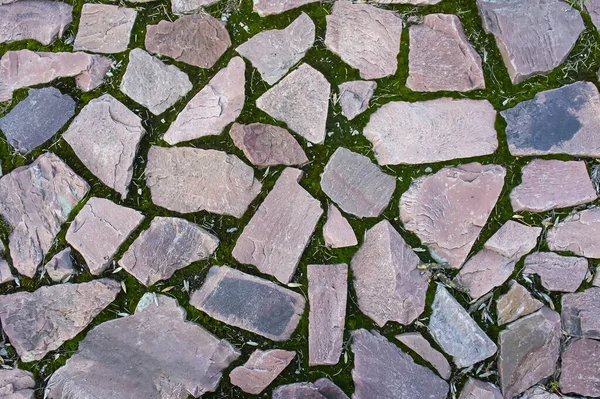 The broken stones of the sidewalk lie on the ground. Ancient paving stones underfoot. Red granite. Stone paving wall background