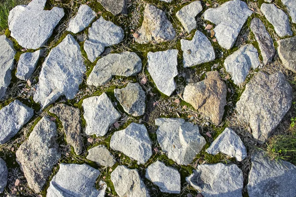 The broken stones of the sidewalk lie on the ground. Ancient paving stones underfoot. Red granite. Stone paving wall background