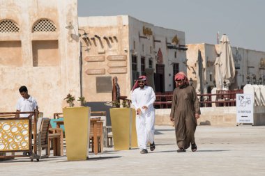 Doha ,Qatar - February 01,2020 : New souk Al Wakrah waterfront promenade with his traditional housesand local people enjoying walking. clipart