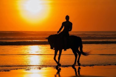 Seminyak Sahili, Bali, Endonezya 'da gün batımında at sırtında bir adamın silueti.