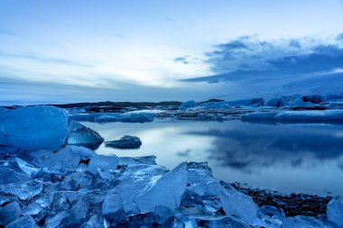 Akşamları buz dağlarındaki İzlanda Buzulu Jokulsarlonu dramatik gökyüzü ile günbatımından sonra soğuk ve huzurlu suda yüzer.