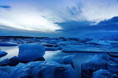Akşamları buz dağlarındaki İzlanda Buzulu Jokulsarlonu dramatik gökyüzü ile günbatımından sonra soğuk ve huzurlu suda yüzer. .
