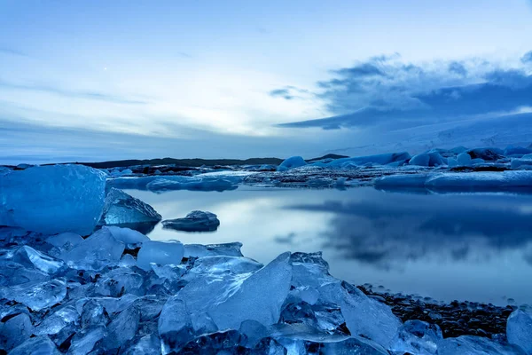 Akşamları buz dağlarındaki İzlanda Buzulu Jokulsarlonu dramatik gökyüzü ile günbatımından sonra soğuk ve huzurlu suda yüzer.
