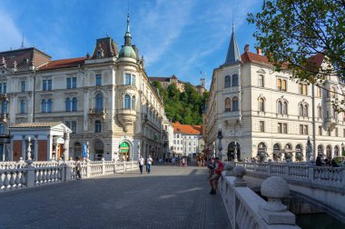 09.08.2021: Ljubljana, Slovenya: Ljubljana, Slovenya: Tromostovje ile Ljubljanica nehri üzerindeki Preseren Meydanı ve Ljubljanski kalesi Ljubljanski mezunu Laibacher Schloss şehir merkezinde insanlarla .