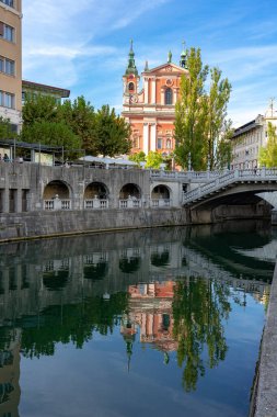 Slovenya 'daki Ljubljanica nehri üzerindeki Tromostovje köprüsü ile Preseren Meydanı ve nehir kıyısındaki Cerkev Marijinega oznanjenja kilisesi .