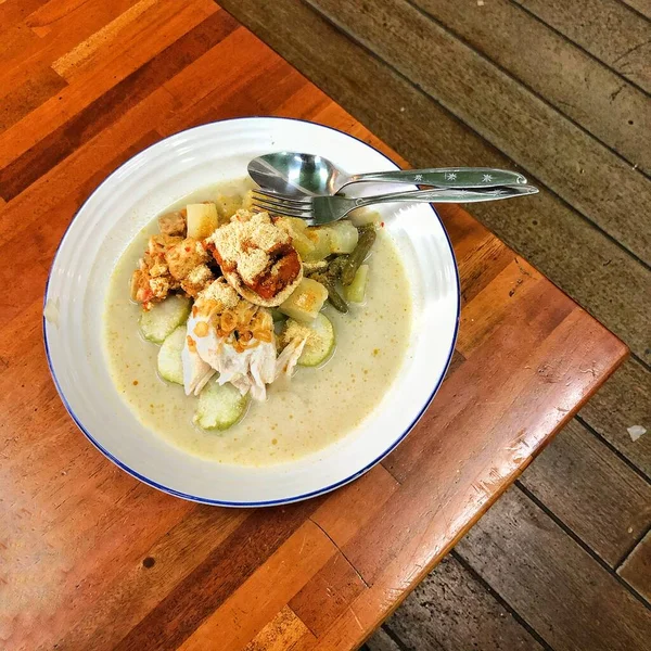 Lontong şapkası Gomeh Endonezya 'da geleneksel bir yemektir. Tahta masadaki bir tabakta servis ediliyor..