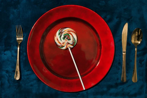 Kırmızı tabakta büyük tatlı lolipopu mavi kadife çatal bıçaklı. Tatlı bir akşam yemeği için sakin bir hayat.