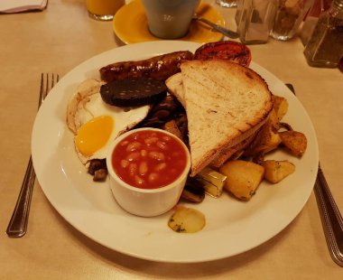 Tam bir İngiliz kahvaltısı pastırma, sosis, yumurta, siyah puding, fırında fasulye, domates, mantar, tost ekmeği ve bir fincan kahve içerir. Londra, İngiltere, Birleşik Krallık.