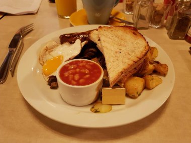 Tam bir İngiliz kahvaltısı pastırma, sosis, yumurta, siyah puding, fırında fasulye, domates, mantar, tost ekmeği ve bir fincan kahve içerir. Londra, İngiltere, Birleşik Krallık.