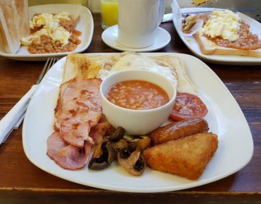 Geleneksel İngiliz kahvaltısı domuz pastırması, sosis, yumurta, fırında fasulye, domates, mantar, tost ekmeği ve bir fincan kahve. Londra, İngiltere, Birleşik Krallık.