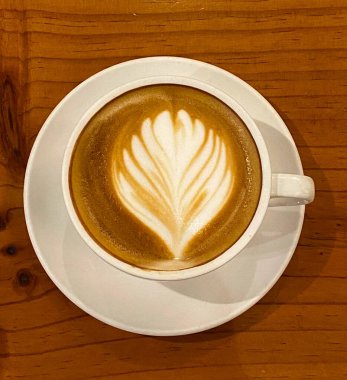 Çiçekli latte sanatıyla süslenmiş bir fincan sıcak latte..