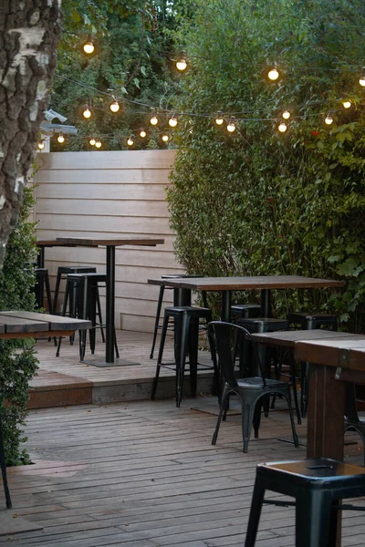 Tahta masaları ve metal siyah sandalyeleri olan bir bar. Sarı ışıklar.