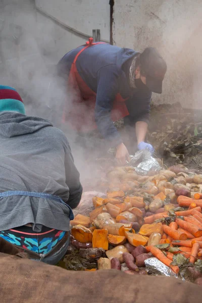 woman and man cooks preparing and serving vegetables and meats cooked under the ground