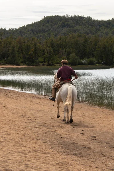 Kumlu ve dağlı bir gölün yanında ata binen beceriksiz Patagonya Arjantin