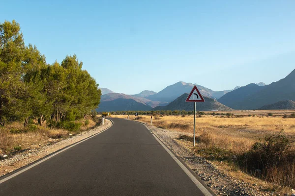 Arka planda ağaçlar ve dağlar olan bir sonraki kavis işareti olan siyah yol