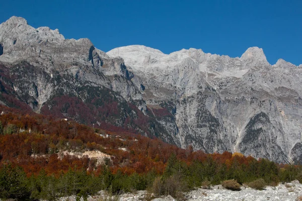 Arnavutluk 'un Theth Alplerinde mevsimlik renklere sahip açık mavi gökyüzü ve ağaçlarla sonbaharın başında güzel dağ manzarası