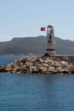 Türkiye 'nin Kas kentindeki küçük deniz feneri, kayalarda oturan iki gölge, dağların arka plan görüntüsü. 