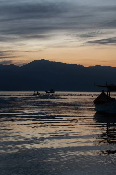 Denizin üzerinde inanılmaz bir gün batımı, arka planda küçük kayıklar ve tepeler, Caieira da Barra do Sul 'da, 