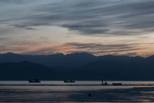Denizin üzerinde inanılmaz bir gün batımı, arka planda küçük kayıklar ve tepeler, Caieira da Barra do Sul 'da, 