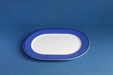 Mavi stüdyo arka planında geometrik çizgilerle süslenmiş boş bir tabak. Tablo takımı ve ev servisi.