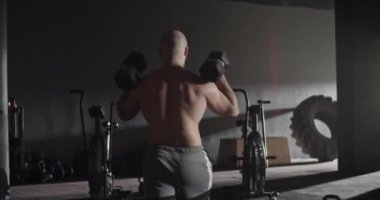 Formda olmayan sporcu dambıllarla hamle yapıyor.