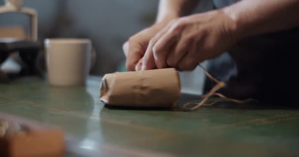 Male artisan wrapping parcel on table — Stock Video