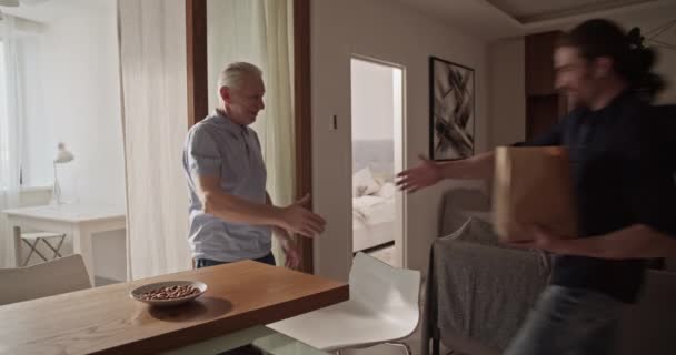 Erwachsener Sohn Bringt Papiertüte Mit Geschenk Und Grüßt Senior Papa — Stockvideo