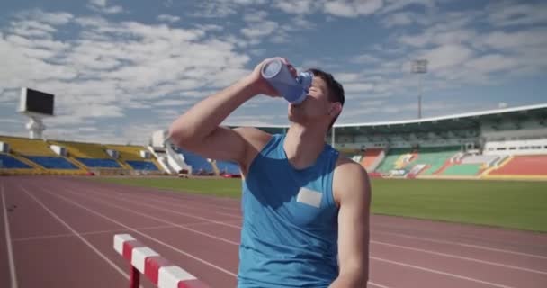 运动员坐在竞技场的障碍物上 从瓶子里喝水 — 图库视频影像