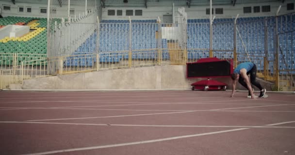 陸上競技場でレーストラックを走らせながら障害物を飛び越えるスポーツマン — ストック動画