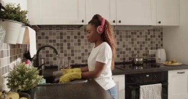 Afro-Amerikalı kadın bulaşık yıkarken ıslak bardağı inceliyor.