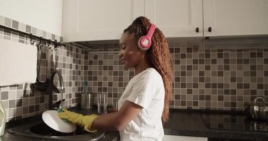 African American woman listening to music and washing plate at home