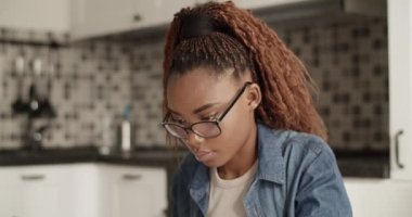 Young black woman writing down data from tablet while studying at home