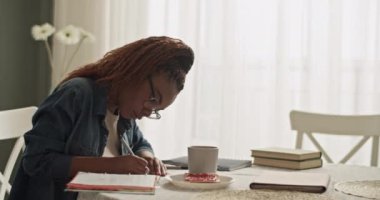 Black woman writing in planner near toast and coffee during studies