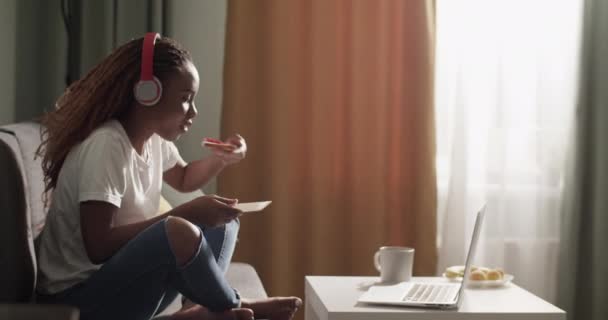 Glad Black Woman Biting Toast Watching Film Laptop Home — Wideo stockowe