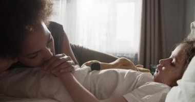 Black mom kissing hand of kid with plush toy and talking in morning