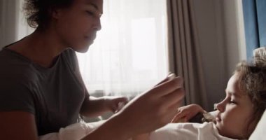 Black mom talking with daughter while measuring temperature of child