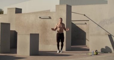 Athlete doing jumping jacks near concrete wall during aerobic training