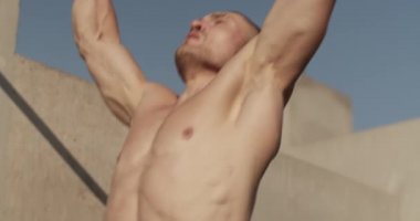 Muscular male athlete doing pull up exercise on bar on street