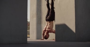 Shirtless male athlete doing handstand push ups near concrete wall