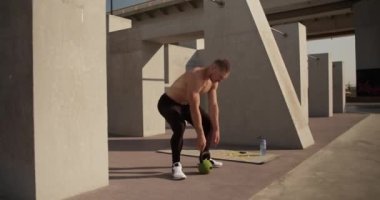 Erkek atlet ağır kettlebell alıyor ve çömelmeye başlıyor.