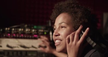Black vocalist controlling soundboard and singing in recording studio