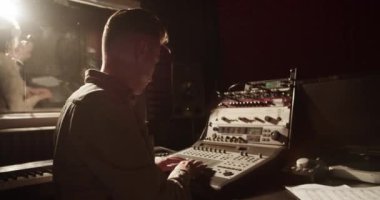 Man using mixing console while black woman singing in record studio