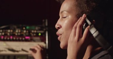 Black vocalist controlling soundboard and singing in recording studio
