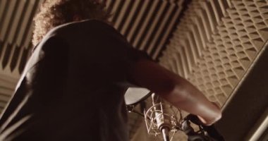 Black woman putting on headphones near microphone in recording studio