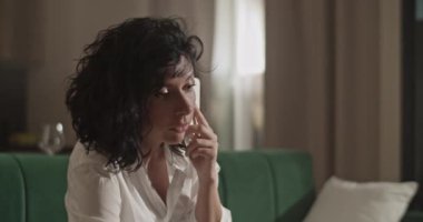 Adult female architect browsing data on netbook and correcting draft while sitting on sofa and talking with boss via smartphone at home.