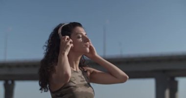 Genç bir bayan dansçının kablosuz kulaklıklarını çıkartıp saçlarına dokunurken elde çekilmiş bir fotoğrafı. Sabahları şehrin caddesinde durup kameraya bakarken.