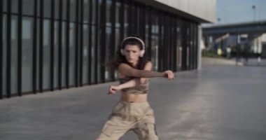 Şık giyinmiş, kablosuz kulaklıkla müzik dinleyen ve hafta sonu şehir caddesinde gösteri yaparken el kol hareketleri yapan esnek kadın dansçıya bakın.